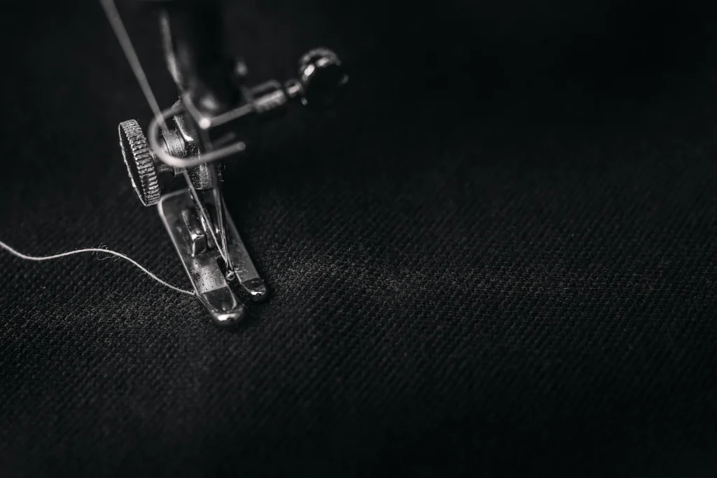 Pied-de-biche et fil blanc sur un tissu sombre pendant une couture à la machine