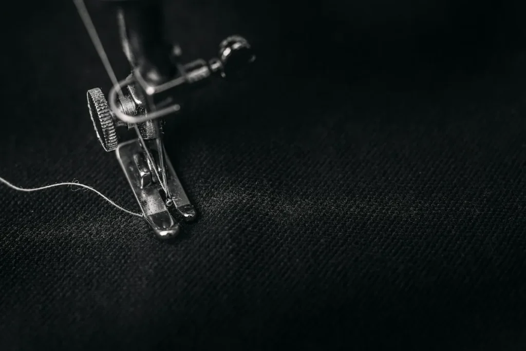Gros plan du pied presseur et de l’aiguille d’une machine à coudre avec le fil sur un tissu noir